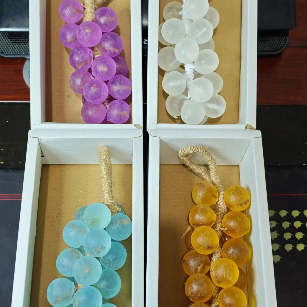Four clusters of glass grapes in purple, white, blue, and amber, in white boxes.