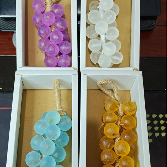 Four clusters of glass grapes in purple, white, blue, and amber, in white boxes.