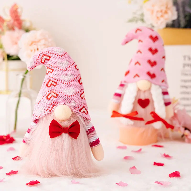 Two gnomes with pink heart hats and red bows, surrounded by flowers and rose petals.