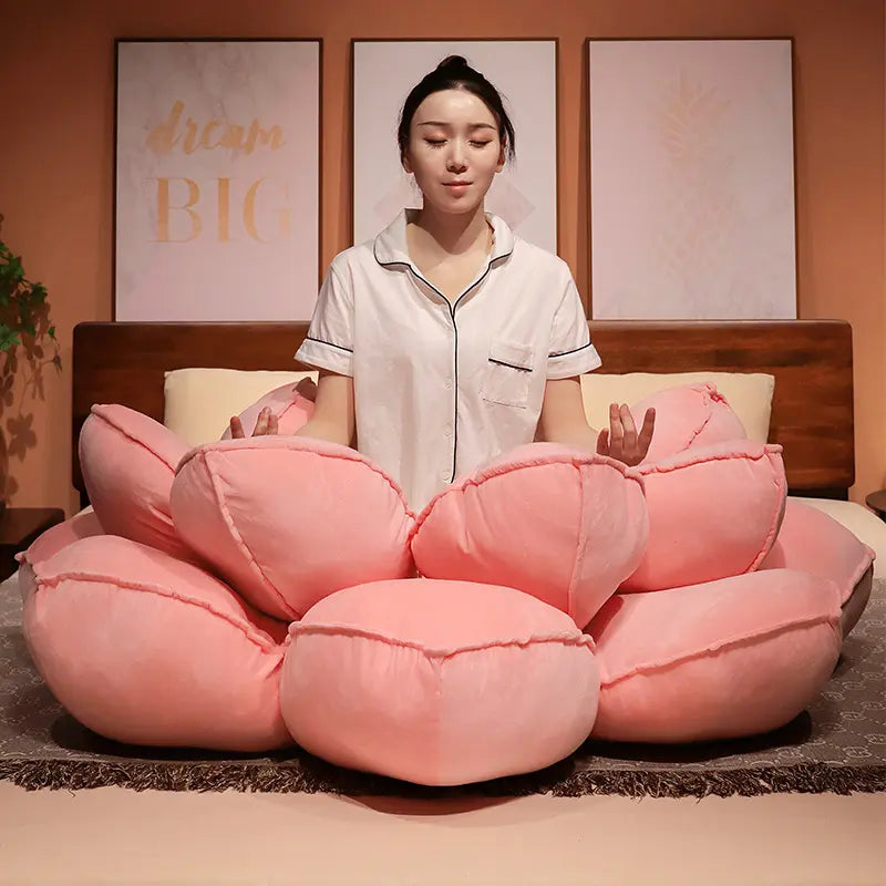 Woman meditating on a bed of large pink petal cushions in a warmly lit room.
