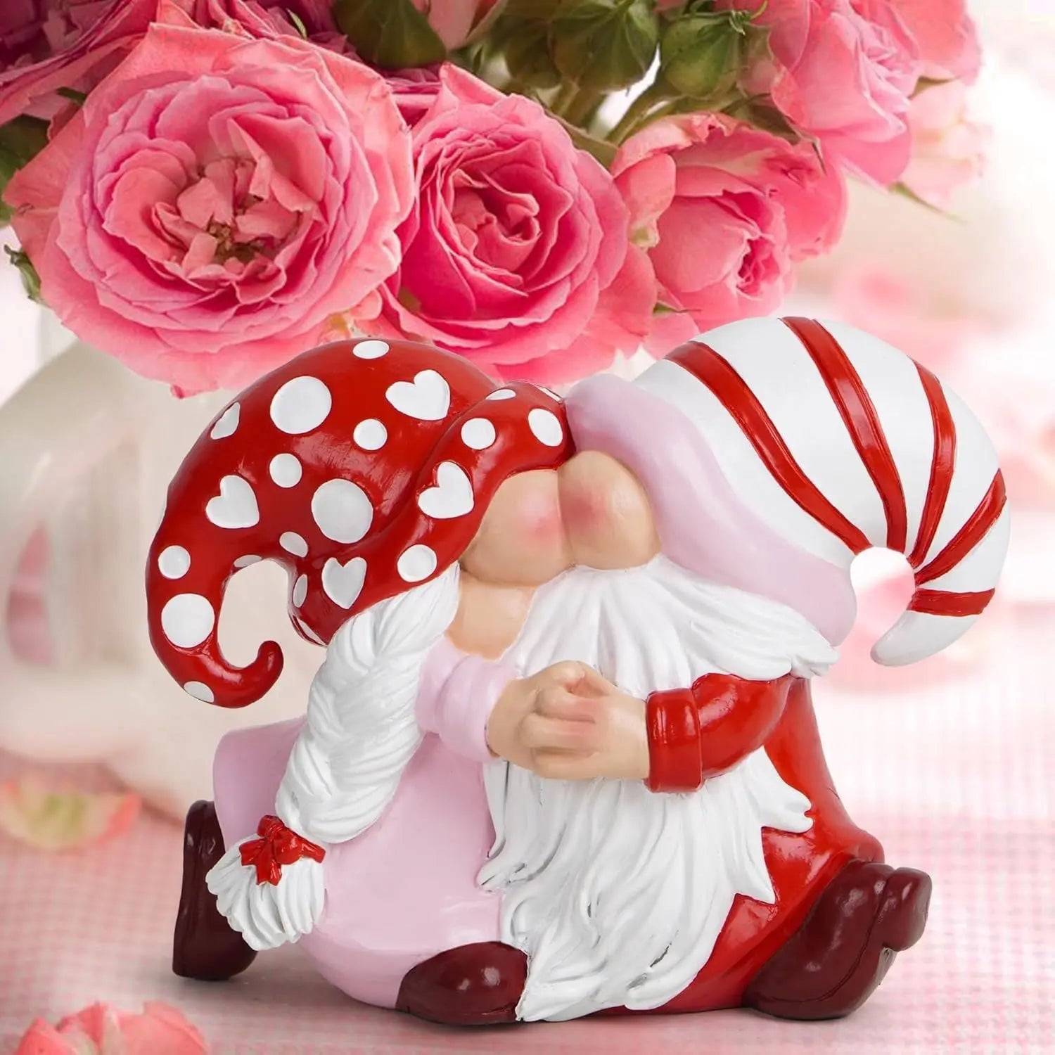 Two gnomes with red and white hats kiss, surrounded by pink roses on a checkered cloth.