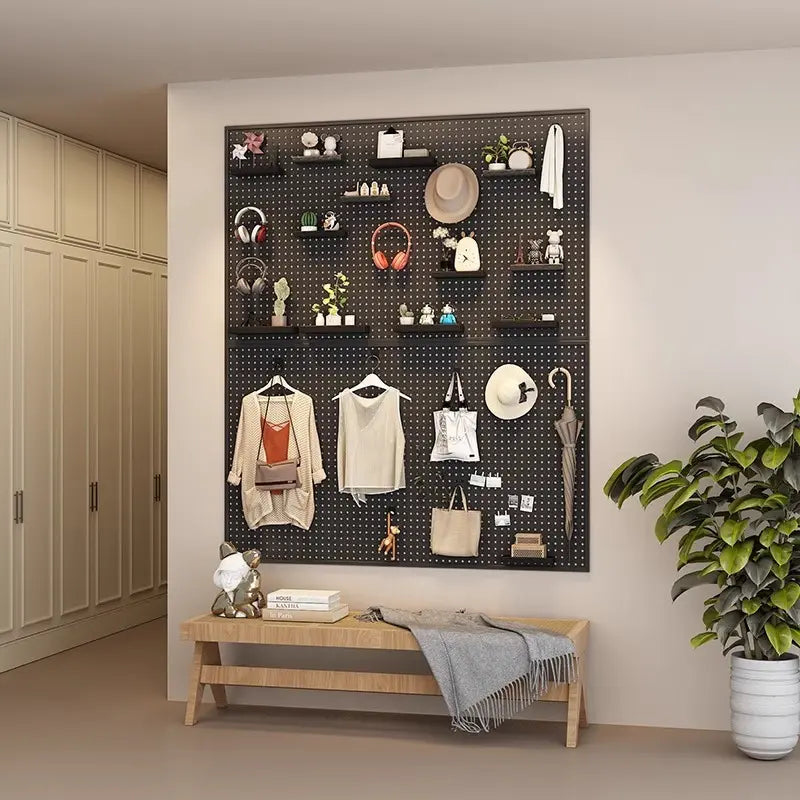 Wall-mounted black pegboard with accessories, clothes, and decor above a wooden bench.