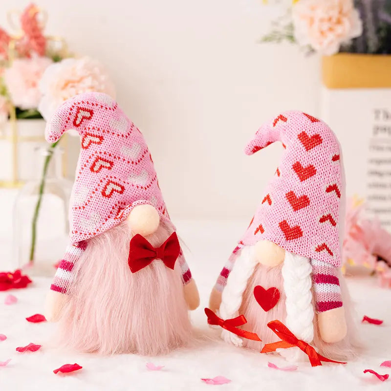 Two gnomes with pink hats and hearts, one with a bow tie, surrounded by flowers and petals.