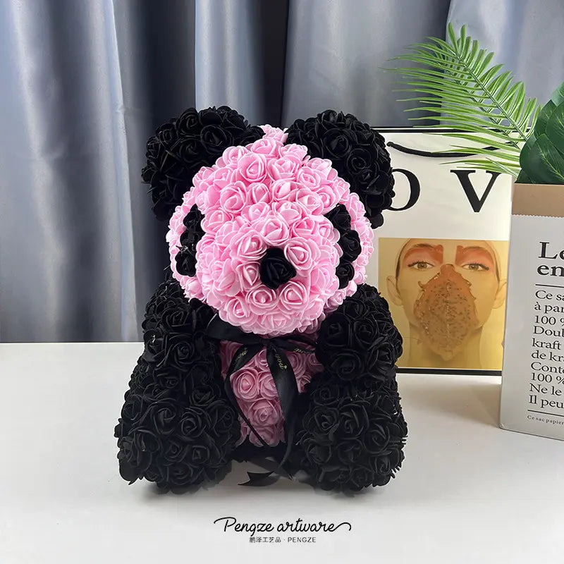 A panda bear made of pink and black roses sits on a table with books and a plant nearby.