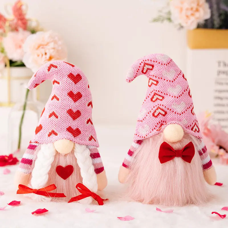 Two gnomes with pink hats, heart patterns, and red bows, surrounded by flowers and petals.