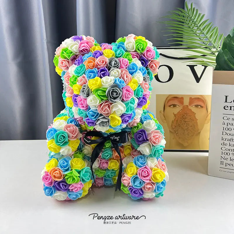 Colorful teddy bear made of small roses, with a black bow, placed on a white surface.