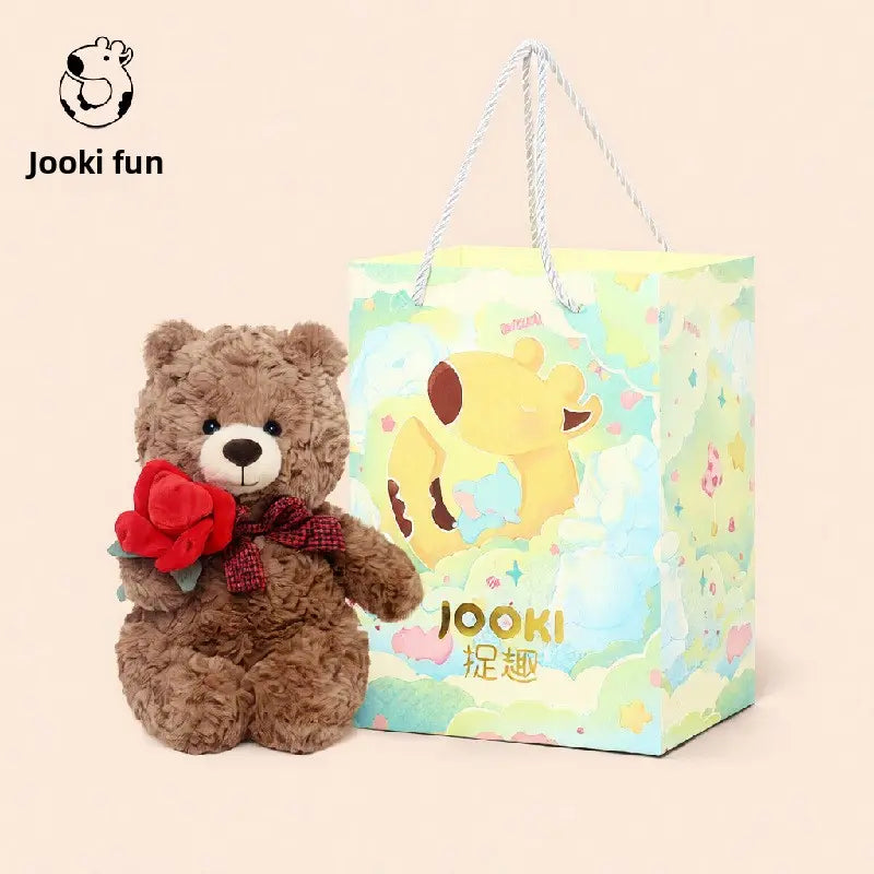 A brown teddy bear with a red bow sits next to a colorful gift bag with cute animal designs.