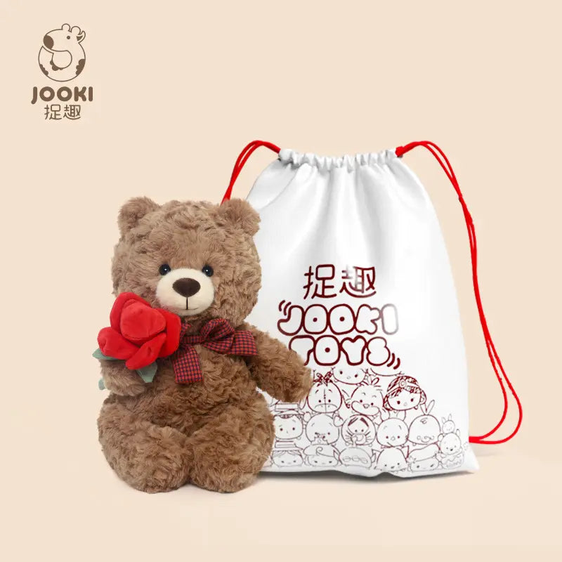 A brown teddy bear holding red roses beside a white drawstring bag with red illustrations.