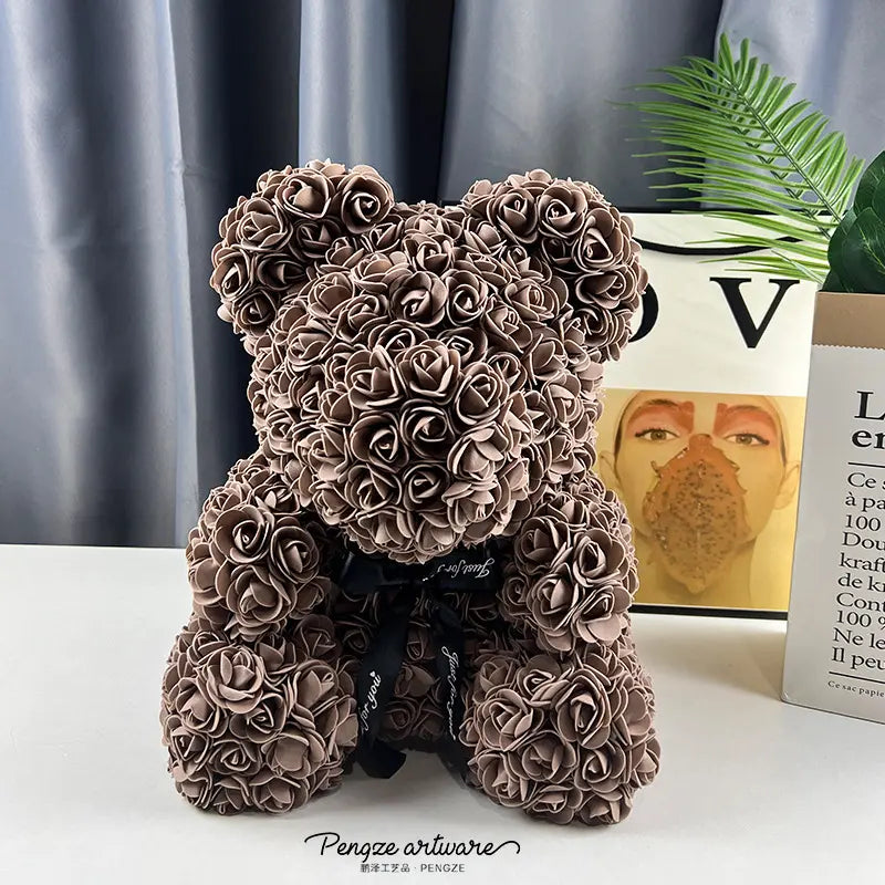 Brown rose-covered teddy bear with a black ribbon, set against a gray curtain and book background.