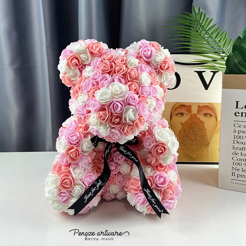 Teddy bear made of pink and white roses with a black ribbon, set on a white table.
