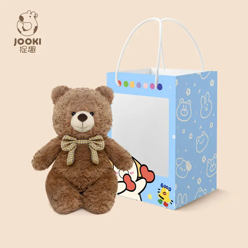 A brown teddy bear with a bow sits beside a blue gift bag with cute cartoon designs.