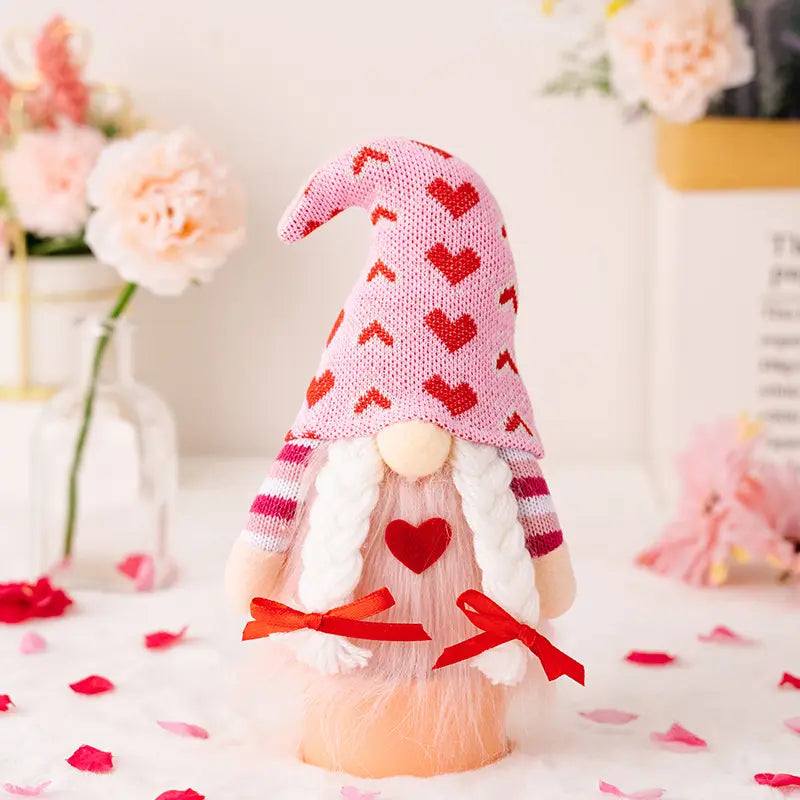 A gnome with a pink heart hat, white braids, and red bows, surrounded by flowers and petals.
