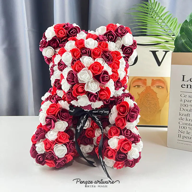 A teddy bear made of red, white, and pink roses, with a black ribbon, on a table near a plant.