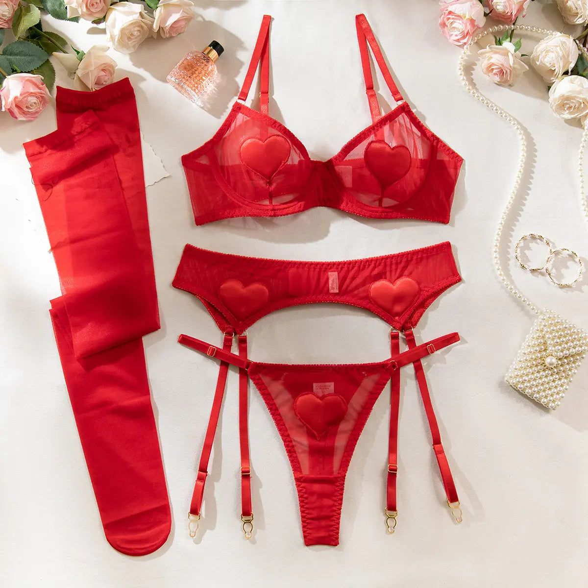 Red lingerie set with heart details, garter belt, stockings, and roses. Pearls and a perfume bottle nearby.