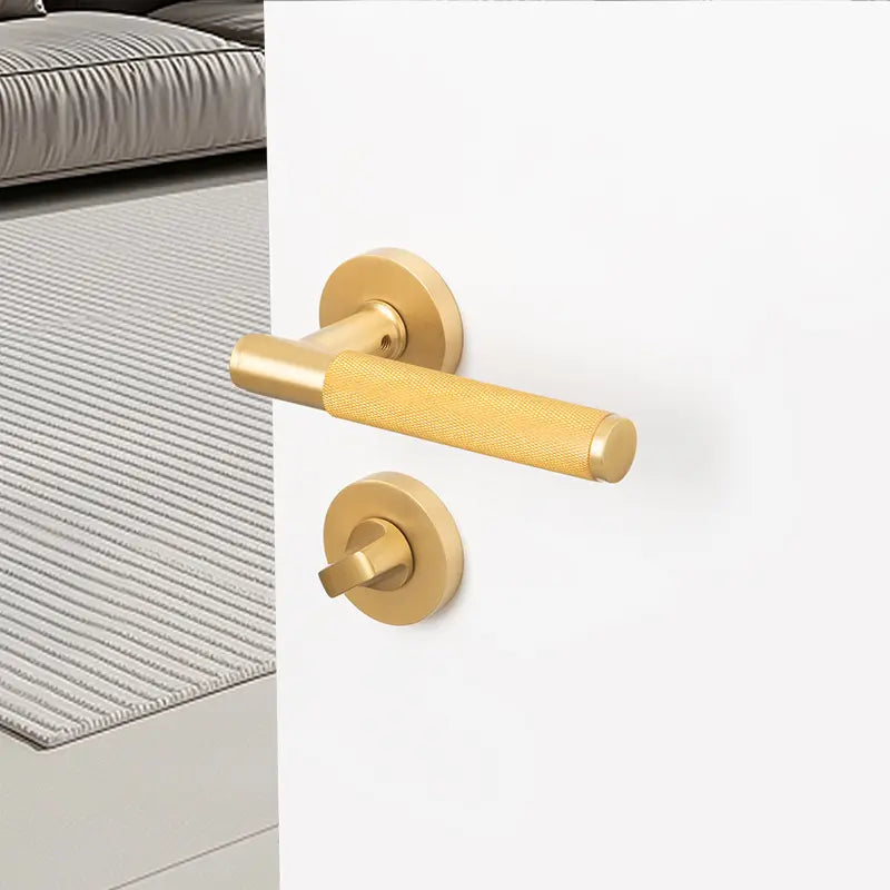 Gold door handle on white door, with a bed and striped bedding in the background.
