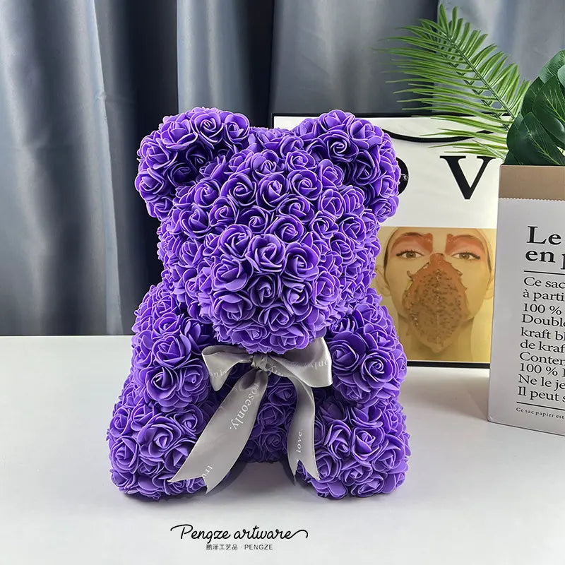 Purple rose bear with silver bow on a table, gray curtain and plant in the background.