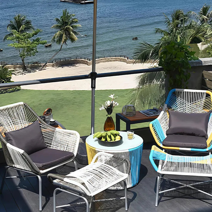 Outdoor patio with wicker chairs, colorful cushions, a table with fruit, overlooking a beach and ocean.