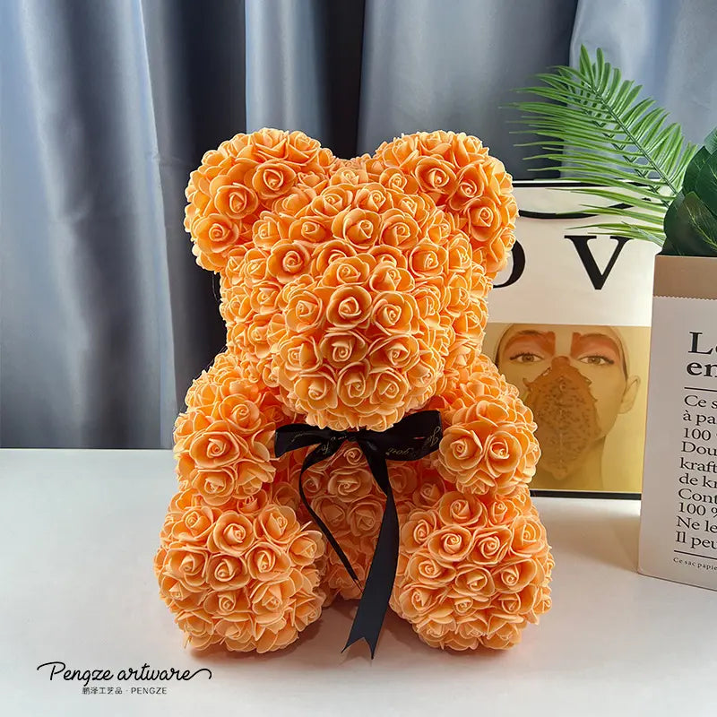 Orange rose-covered teddy bear with black bow, set against a gray curtain and green plant.