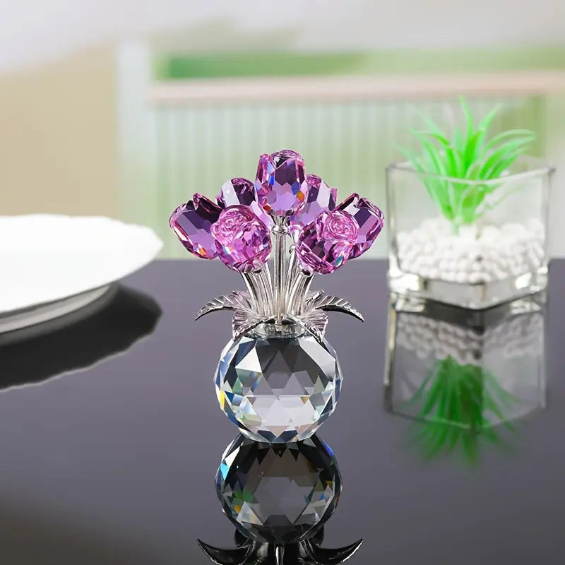 Crystal vase with purple flowers on a reflective black surface, green plant in the background.