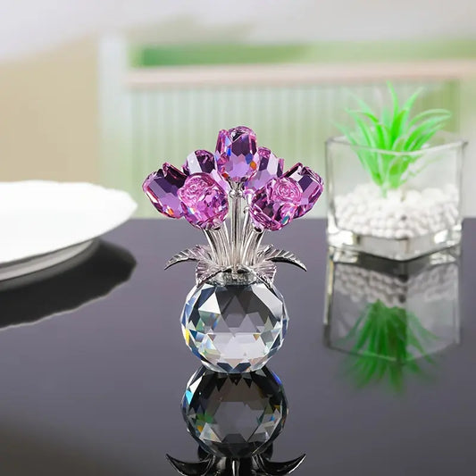 Crystal vase with purple flowers on a reflective black surface, green plant in the background.