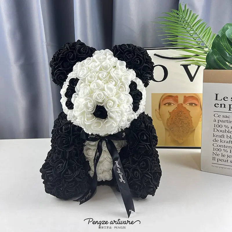 Panda-shaped sculpture made of black and white roses, with a black ribbon, set on a white surface.