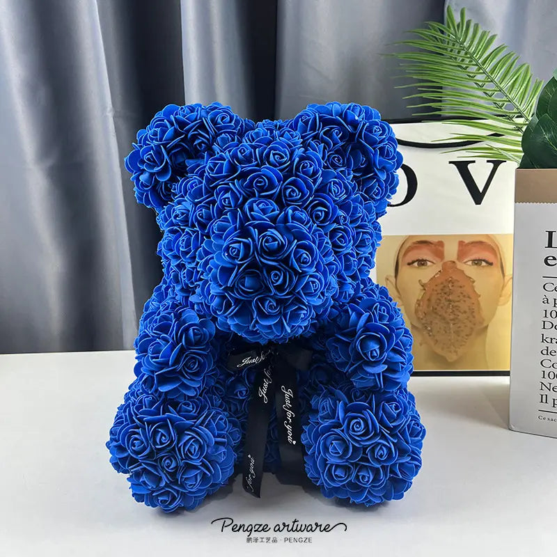 Blue teddy bear made of roses on a white surface with a gray curtain and books in the background.
